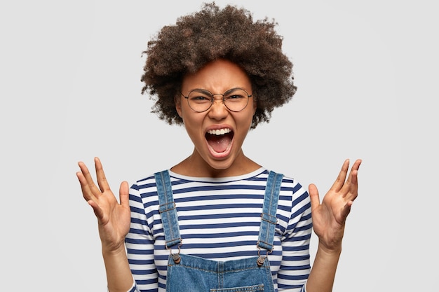 Photo gratuite jeune femme à la peau sombre furieuse fait des gestes avec colère et regarde avec agacement