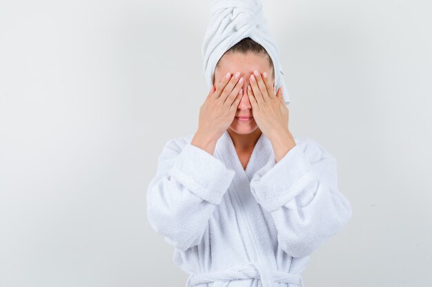 Jeune femme en peignoir blanc, serviette couvrant les yeux avec les mains et à la vue de face, plein de ressentiment.