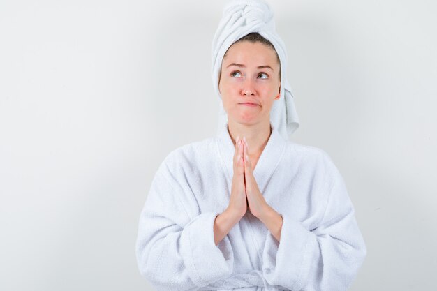 Jeune femme en peignoir blanc, serviette tenant par la main en signe de prière et à la recherche d'espoir, vue de face.