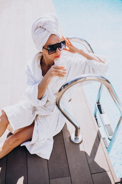 Jeune femme en peignoir, boire du café au bord de la piscine