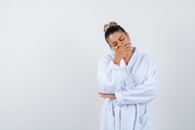 Jeune femme en peignoir couvrant la bouche avec la main et à la somnolence