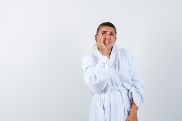 Jeune femme en peignoir mettant la main sur la joue et à la pensive