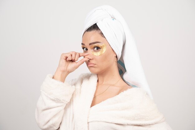 Jeune femme en peignoir et patchs oculaires cosmétiques posant