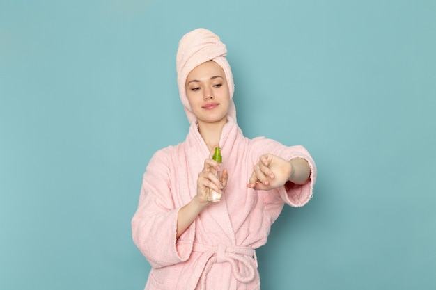 Photo gratuite jeune femme en peignoir rose à l'aide de spray corporel sur bleu