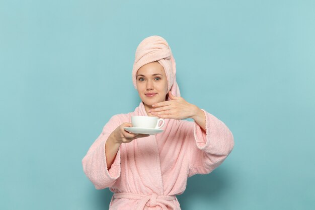 Jeune femme en peignoir rose après la douche, boire du café souriant sur bleu
