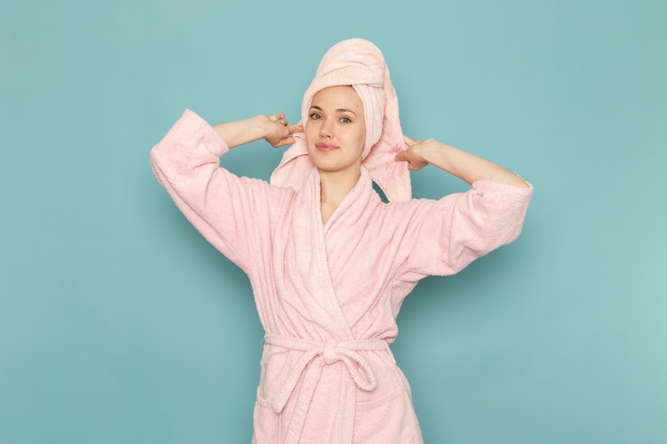 Photo gratuit jeune femme en peignoir rose après la douche souriant sur bleu