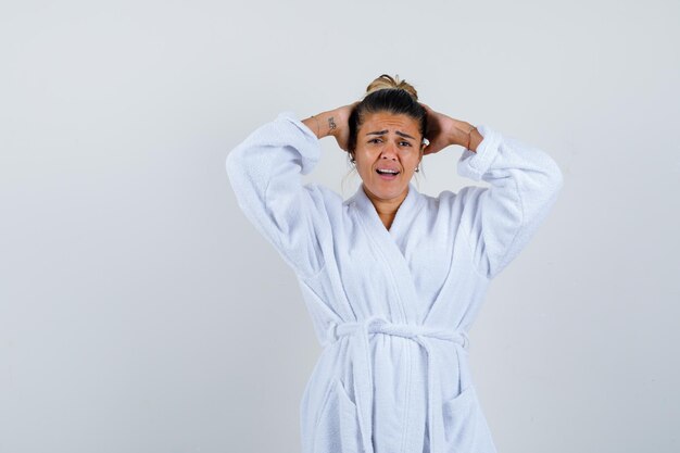 Jeune femme en peignoir tenant les mains derrière la tête et à la confusion