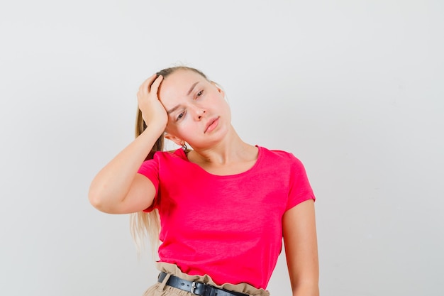 Jeune femme penchant la tête sur la paume surélevée en t-shirt rose et à la pensif