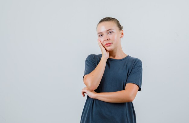 Jeune femme penchée joue sur la paume surélevée en t-shirt gris et à la pensive