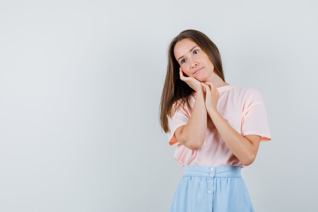 Jeune femme penchée joue sur la paume en t-shirt, jupe et à la pensive, vue de face.