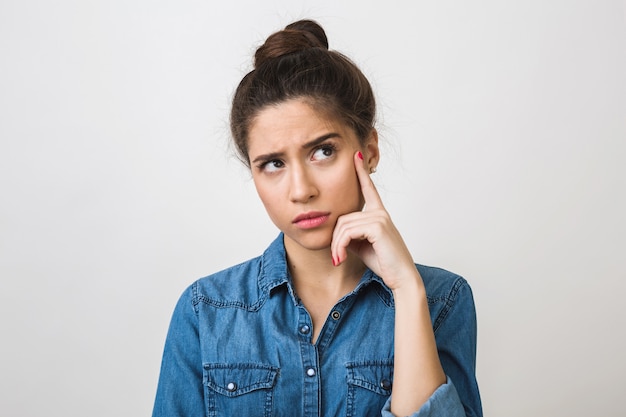 Jeune femme pensant, tenant le doigt sur sa tempe, regardant vers le haut, chemise en jean élégant,