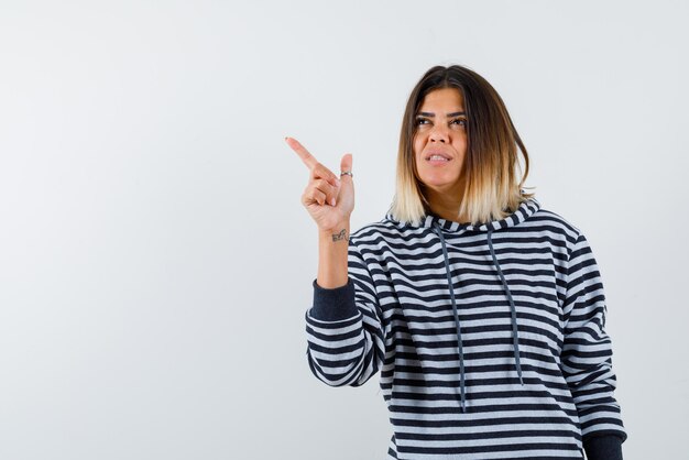 La jeune femme pensante pointe vers la gauche avec l'index sur fond blanc