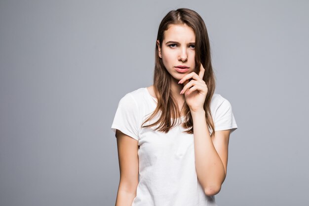 Jeune femme pensante en t-shirt blanc et jeans bleu rester devant un fond de studio blanc