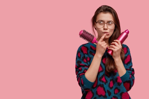 Une jeune femme pensive a déplu à une expression indécise, s'est concentrée vers le haut, pense à ses projets futurs, porte des lunettes carrées