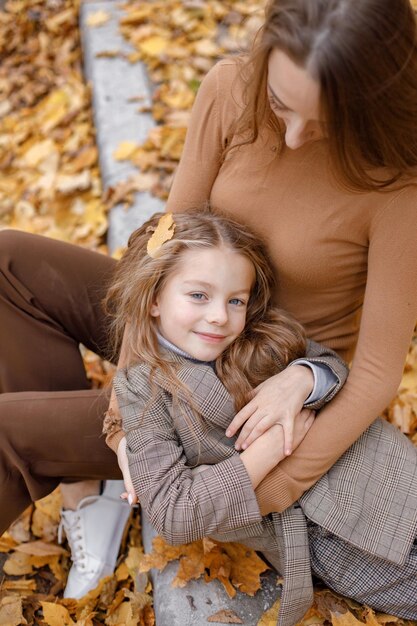 Jeune femme et petite fille dans la forêt d'automne. Femme étreignant sa fille. Fille portant des vêtements de mode et allongée sur les genoux de sa mère.