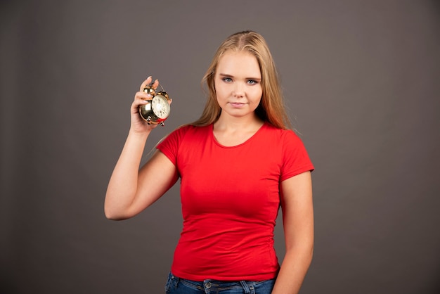 Jeune femme avec une petite horloge debout sur un mur noir.