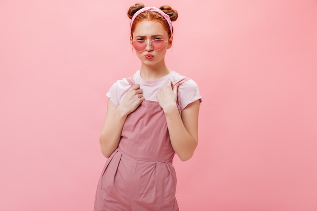 Jeune femme avec des petits pains posant sur fond rose. Portrait de femme à lunettes élégantes, combinaison rose et haut blanc.