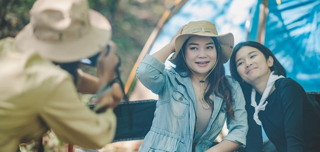 Jeune femme photographe aime prendre des photos avec ses amis, elle utilise un appareil photo numérique et une jolie fille pose à la tente de camping dans l'espace de copie de la forêt naturelle