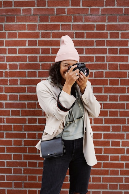 Jeune femme photographe élégante prenant des photos contre le mur de briques dans la ville
