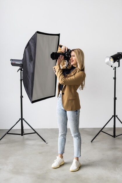 Jeune femme photographe posant dans le studio photo souriant et tenant un appareil photo numérique professionnel