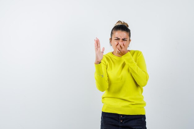 Jeune femme pinçant le nez à cause d'une mauvaise odeur dans un pull jaune et un pantalon noir et ayant l'air ennuyé