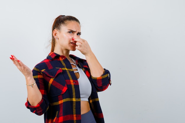 Jeune femme pinçant le nez à cause d'une mauvaise odeur en haut, chemise à carreaux et l'air dégoûtée. vue de face.