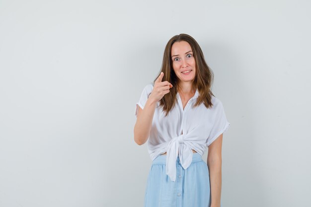 Jeune femme pointant à l'avant en chemisier blanc, jupe bleue et à la recherche concentrée