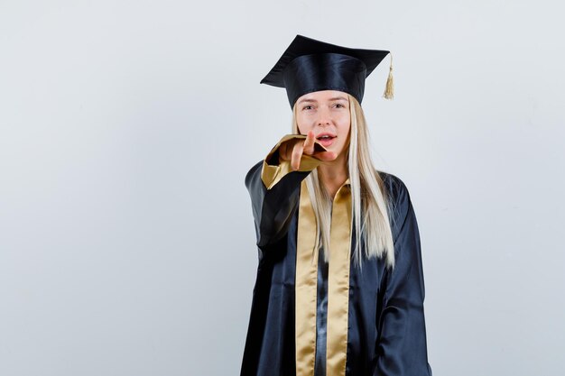 Jeune femme pointant la caméra en robe académique et à la joyeuse