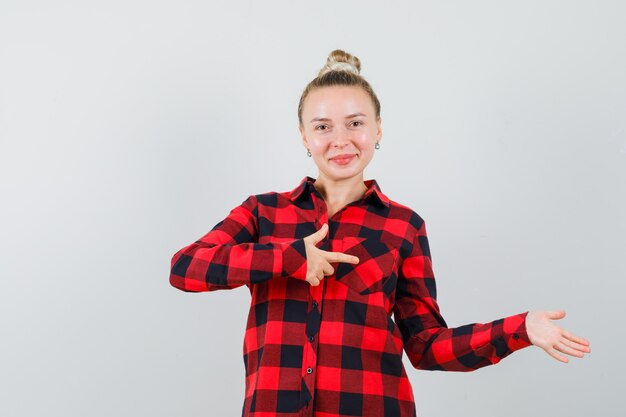 Jeune femme pointant sur le côté en chemise à carreaux et à la joyeuse