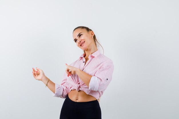 Jeune femme pointant de côté en chemise décontractée, pantalon et à la confiance. vue de face.