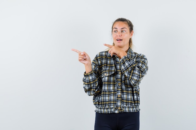 Jeune femme pointant de côté en chemise, short et regardant étonné, vue de face.