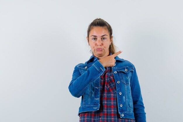 Jeune femme pointant de côté en chemise, veste et à la vue de face, confiant.