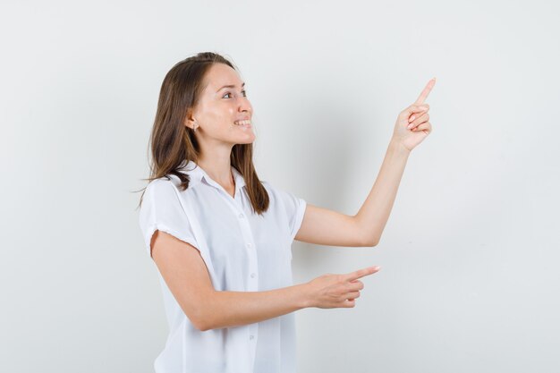 Jeune femme pointant de côté en chemisier blanc et à la joie