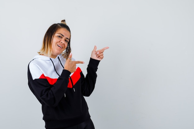 Jeune femme pointant de côté dans un pull à capuche et ayant l'air joyeuse.