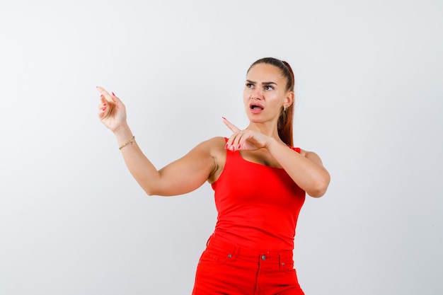 Jeune femme pointant de côté en maillot rouge, pantalon rouge et à la perplexe, vue de face.