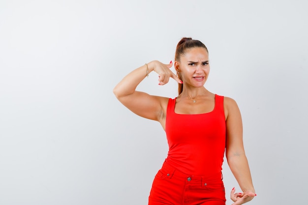 Jeune femme pointant de côté en maillot rouge, pantalon rouge et à la vue indécise, de face.