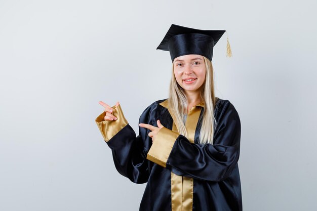 Jeune femme pointant de côté en tenue académique et semblant heureuse