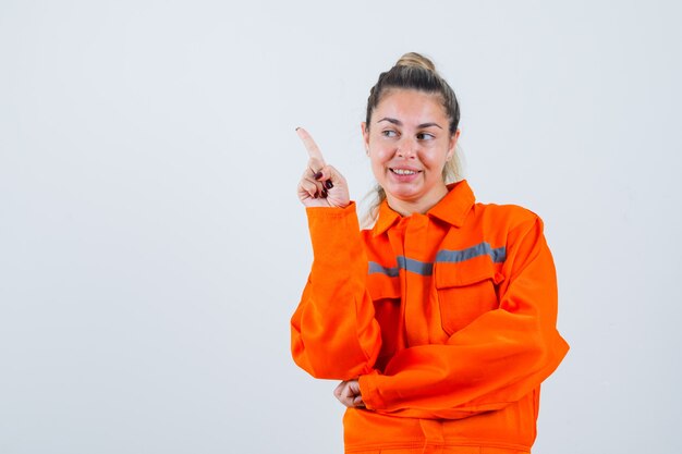 Jeune femme pointant de côté en uniforme de travailleur, vue de face.