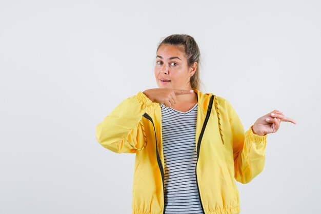 Jeune femme pointant de côté en veste, t-shirt et à la vue de face, confiant.