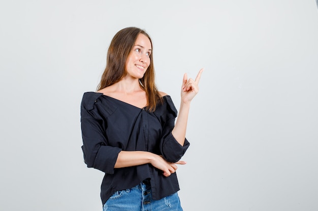 Jeune femme pointant le doigt en chemise, short et à la joyeuse. vue de face.