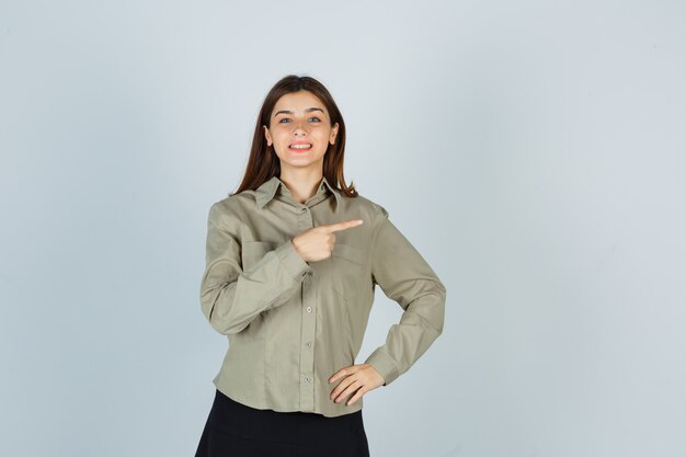 Jeune femme pointant à droite en chemise, jupe et à la joyeuse