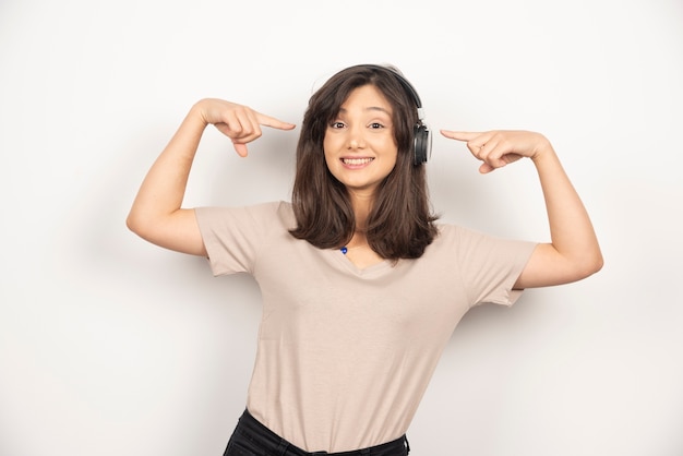 Jeune femme pointant sur les écouteurs sur fond blanc.