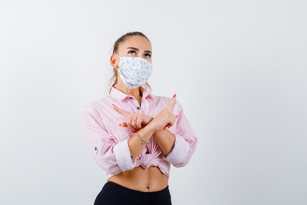 Photo gratuite jeune femme pointant à gauche et à droite en chemise, masque et à hésitant