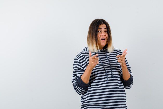 Jeune femme pointant quelque chose avec les doigts loin sur fond blanc