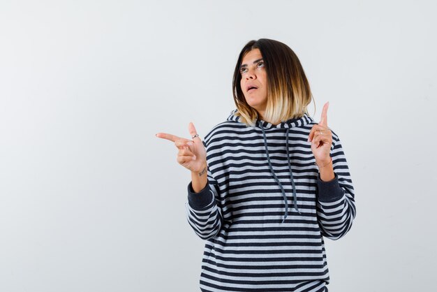 Jeune femme pointant quelque chose en haut et à gauche sur fond blanc