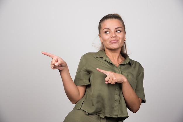 Photo gratuite jeune femme pointant sur son côté sur un mur gris.