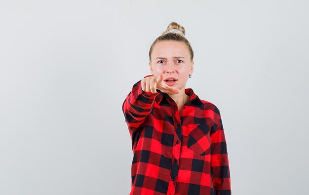 Jeune femme pointant vers l'avant en chemise à carreaux et à l'anxiété