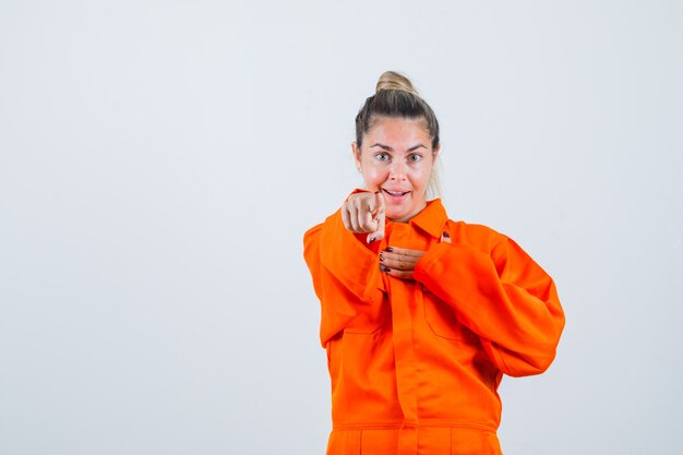 Jeune femme pointant vers l'avant en uniforme de travailleur et à la recherche concentrée. vue de face.