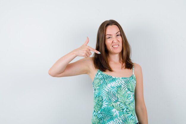 Jeune femme pointant vers le bas en blouse et l'air mécontent , vue de face.