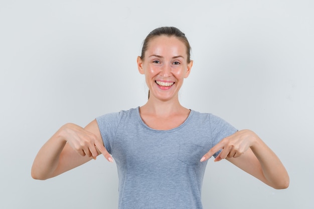 Jeune femme pointant vers le bas et riant en vue de face de t-shirt gris.